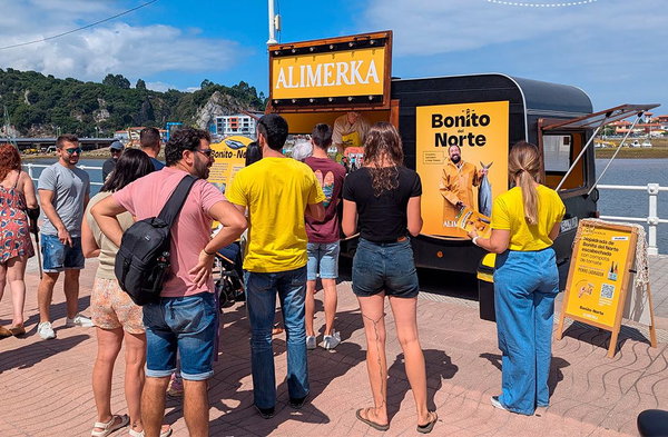 Puesto ambulante ALIMERKA junto a un furgón con carteles Bonito del Norte y personas haciendo cola en el paseo marítimo.