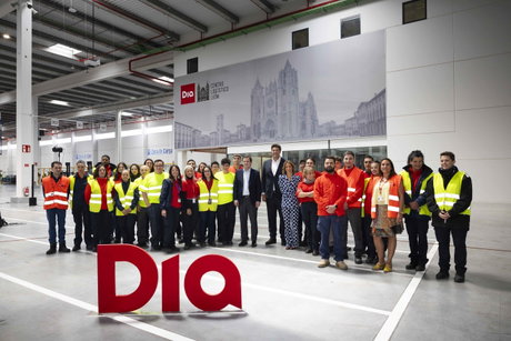 Grupo de empleados y directivos posando en el centro logístico de León con el logo rojo DIA en primer plano.