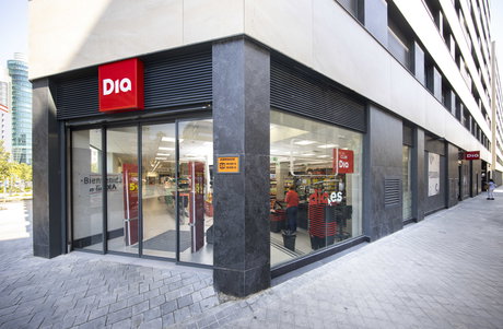 Exterior del supermercado DIA en esquina con entrada acristalada, rótulo rojo y carritos visibles en el interior.