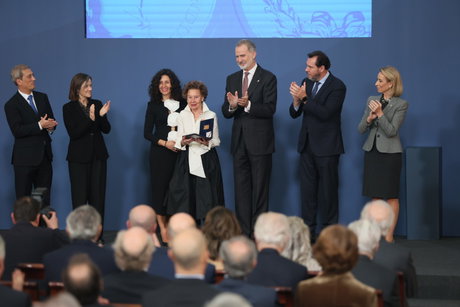Acto de entrega de premio con el rey Felipe VI y autoridades aplaudiendo mientras una mujer sostiene una placa conmemorativa.