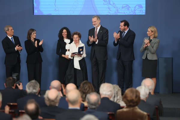 Acto de entrega de premio con el rey Felipe VI y autoridades aplaudiendo mientras una mujer sostiene una placa conmemorativa.