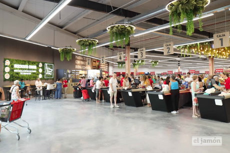 Cajas registradoras con clientes haciendo cola en el supermercado el jamón, mostradores y plantas colgantes decorativas.