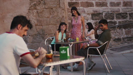 Grupo de jóvenes en terraza de cafetería junto a un muro de piedra, bebidas y un porta-servilletas verde Chovi sobre la mesa.