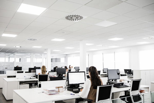 Oficina abierta con puestos de trabajo, personas sentadas y varios ordenadores de sobremesa.