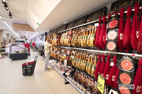 Sección de jamones y paletas colgadas en el lineal de Supermercados El Jamón, cliente seleccionando un jamón.