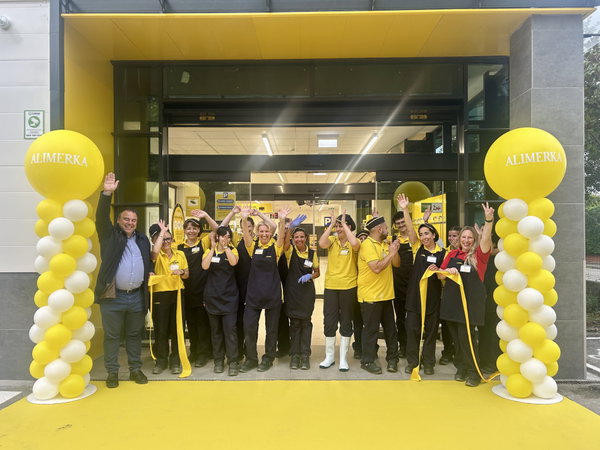 Personal del supermercado ALIMERKA en Somió celebrando la inauguración junto a columnas de globos amarillos y cinta.