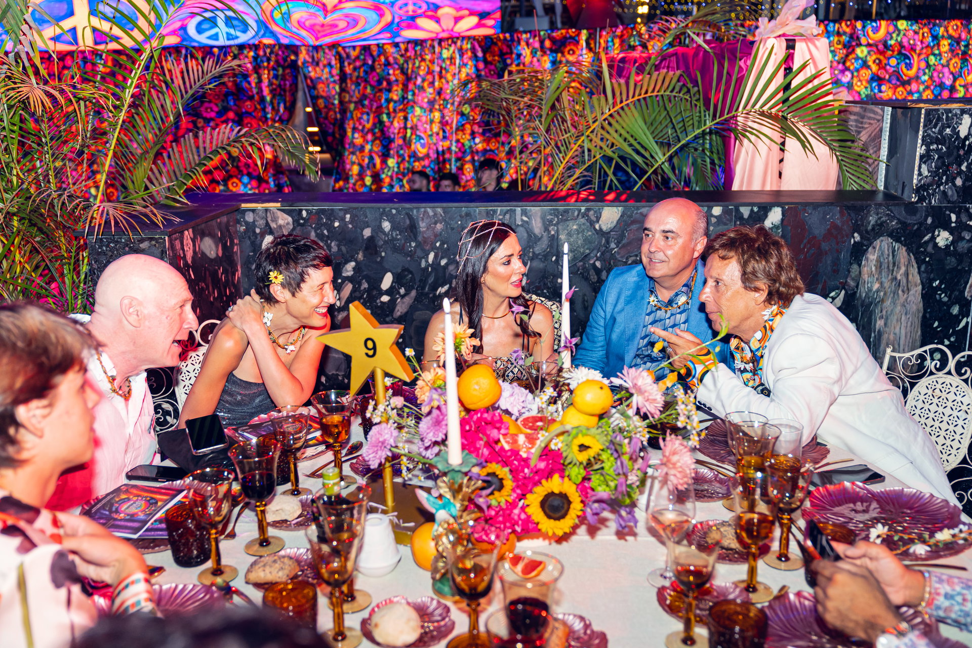 Mesa de gala con invitados conversando en la XVII Gala Starlite Occident, centro floral con frutas, copas y cartel con número