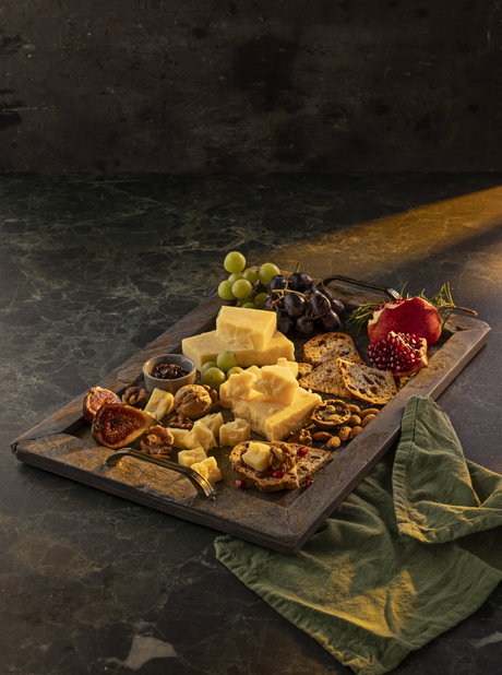 Tabla de quesos curados con uvas verdes y negras, granada partida, higos, nueces y tostas.