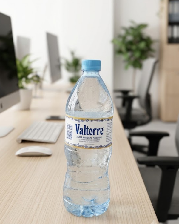Botella de agua Valtorre sobre mesa de oficina con ordenadores y plantas desenfocados.