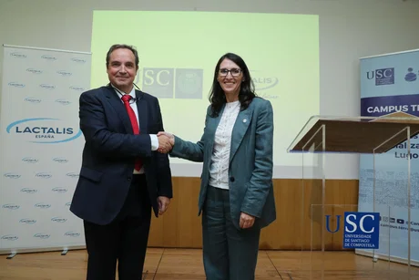 Dos personas, hombre y mujer, estrechan la mano en un acto; al fondo roll-ups y atril con los logos Lactalis y USC.