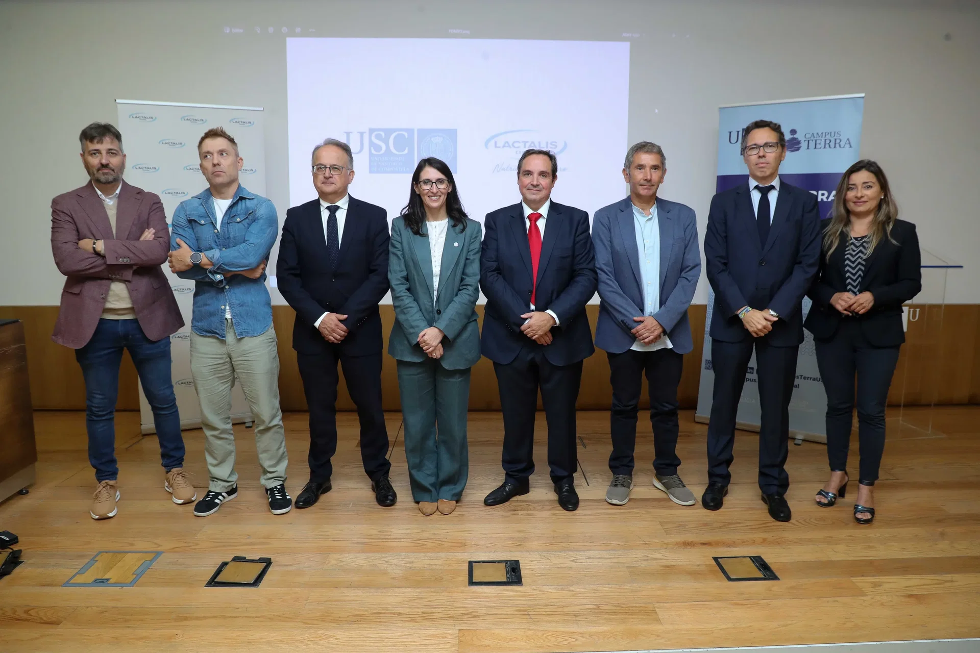 Ocho directivos posan en fila en un escenario con la proyección USC y Lactalis y dos rollups laterales.