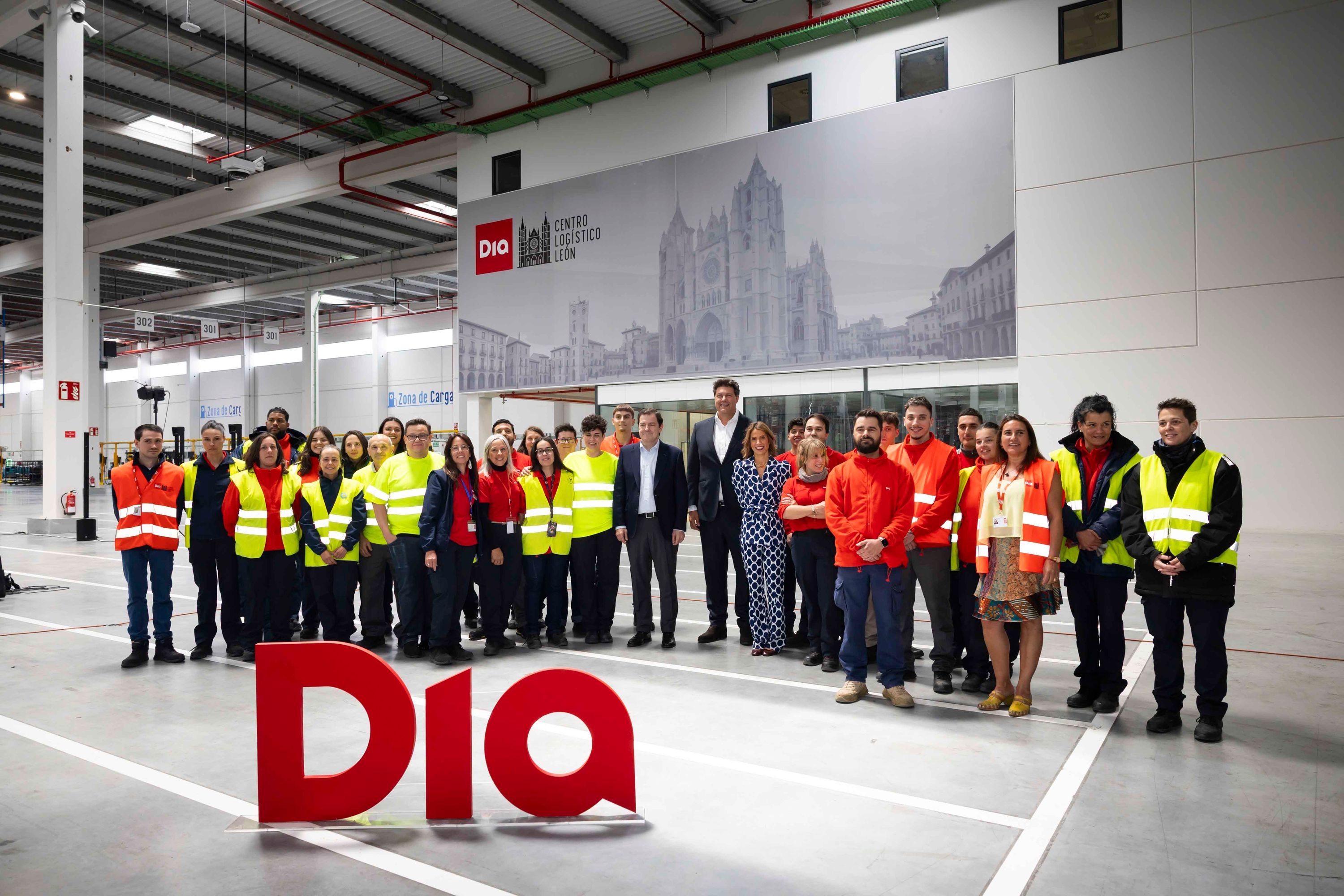 Grupo de empleados y directivos posando en el centro logístico de León con el logo rojo DIA en primer plano.