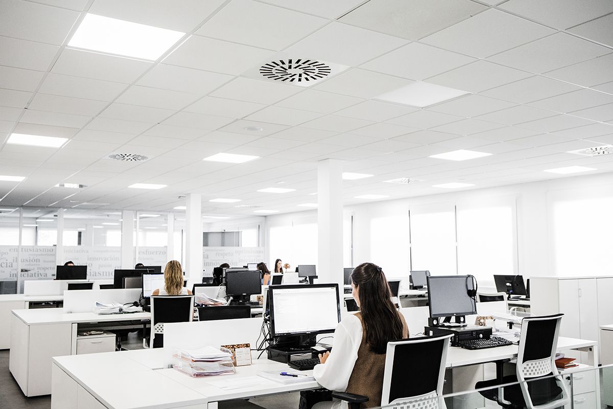 Oficina abierta con puestos de trabajo, personas sentadas y varios ordenadores de sobremesa.
