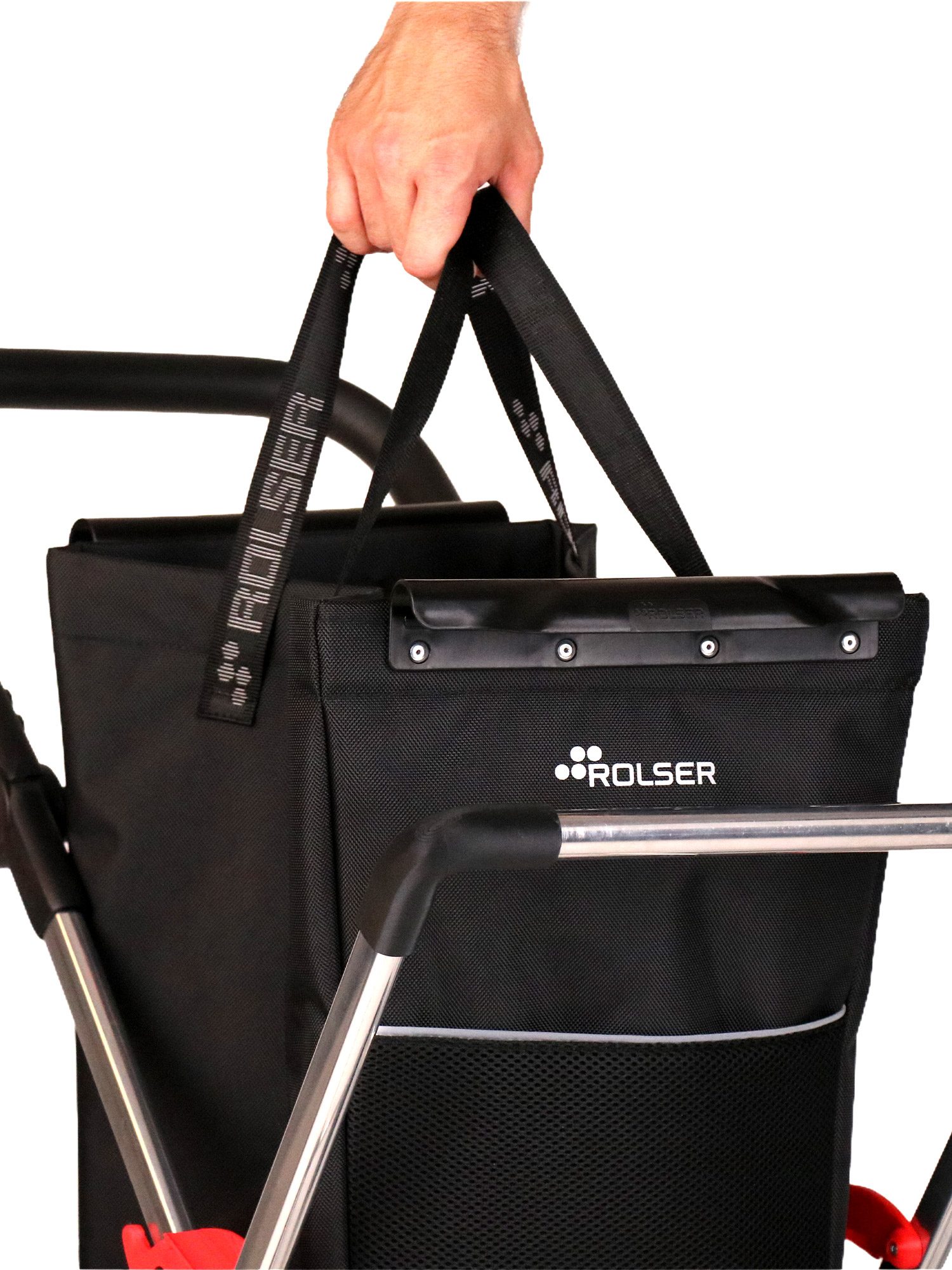 Carrito de la compra ROLSER negro con bolsa textil, bolsillo frontal y asa agarrada por una mano.