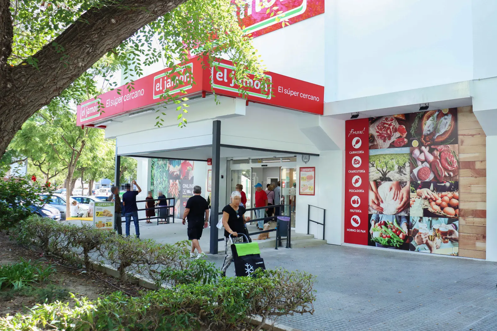 Fachada y entrada del supermercado Supermercados El Jamón con clientes entrando y carro de la compra.